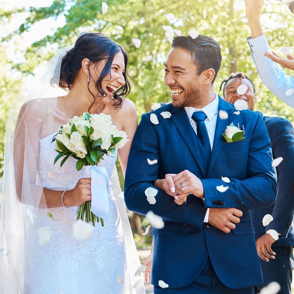 Wedding guests throwing rose petals confetti tradition over bride and groom on their special day. Newlywed couple walking past friends and family