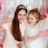 Two girls are having fun at a birthday party with pink balloons and decorations around them. They are smiling and posing happily, enjoying the celebration.